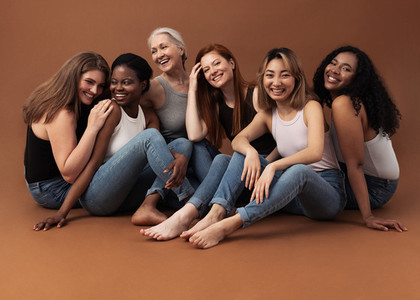 Six women of different ages sitting together in studio on brown background  Multi ethnic group of diverse females having good times