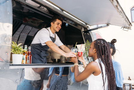 Two customers receiving drinks from food truck owner  Cheerful salesman in apron looking at clients