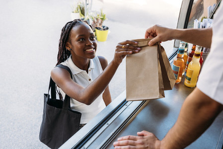 Young cheerful woman receiving takeaway food from a salesman  Unrecognizable food truck owner giving packaged food to a client