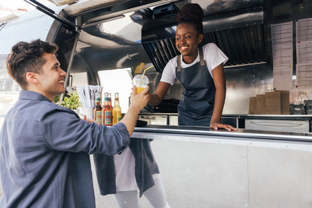 Food truck owner looking at customer  Smiling client receiving a drink from saleswoman