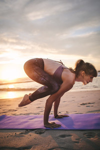 Woman practicing crane pose yoga at beach