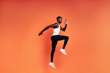 Fit man jumping in studio Male runnner warming up before workout against orange background
