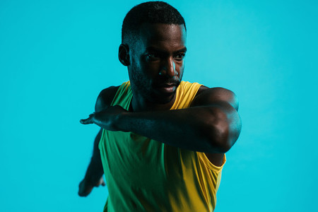 Close up of male athlete stretching arms and body in studio over blue background