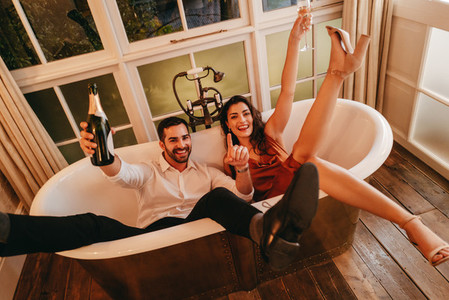 Honeymooners celebrating with sparkling wine in a bathtub
