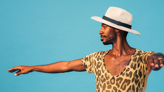 Side view of a young man wearing a straw hat dancing in studio against a blue background