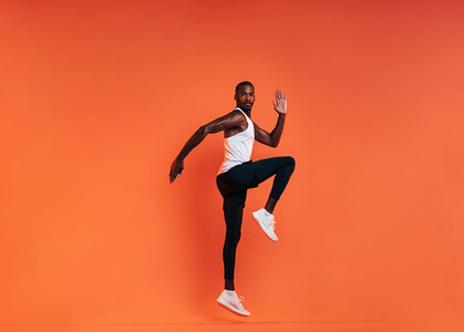 Young fit man doing exercises in studio  Male athlete jumping in the air over an orange background