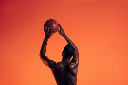 Back view of basketball player against an orange background  Young man in studio preparing to throw basket ball