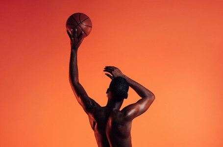 Rearview of basketball player against an orange background  Bare chest athlete holding a basket ball with one hand
