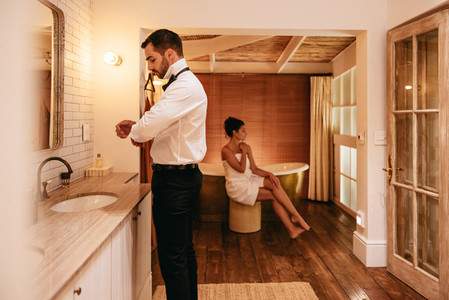 Man getting dressed in a hotel with his wife in the background