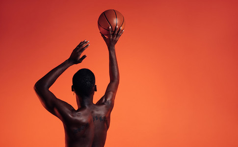 Rear view of a muscular athlete prepare to throw a basket ball in studio