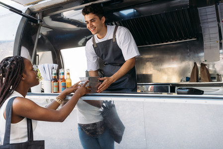 Smiling salesman giving takeaway packaged food to a female customer  Woman taking food from a food truck owner