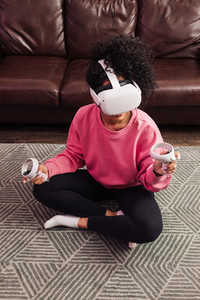 Young woman with curly hair sitting near a sofa and playing VR games