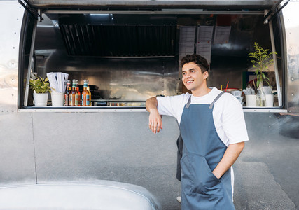 Young business owner in an apron Salesman leaning on a food truck