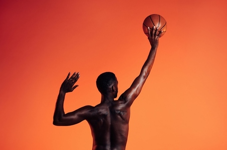 Back view of muscular basketball player exercising against an orange background