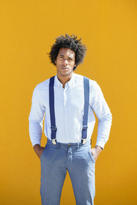 Black man with afro hair on yellow urban background wearing shirt and suspenders