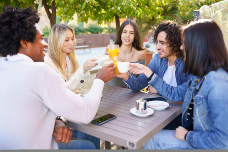 Multi ethnic group of friends toasting with their drinks while having a drink together