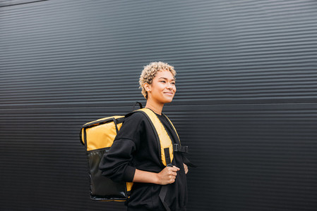 Portrait of delivery girl holding yellow thermal delivery backpack on her back and standing outdoors