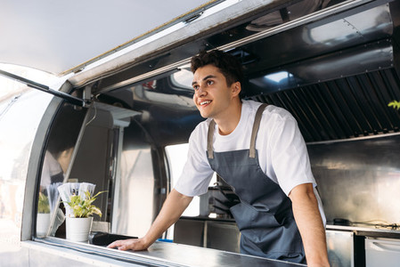 Salesman in apron leaning on a counter in food truck waiting for a clients