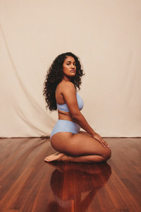 Young woman kneeling while wearing blue underwear in a studio