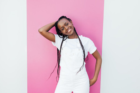 Portrait of a young cheerful girl wearing a white overall standing at wall with pink stripe