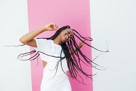 Playful woman with long braided hair dancing at a white wall with pink stripe