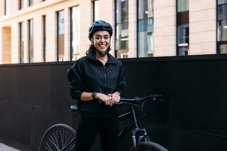 Beautiful smiling woman in black cycling helmet looking at camera while standing in the city