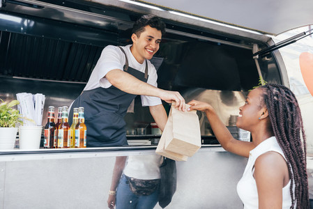 Smiling salesman giving packages with street food to a female customer  Food truck owner serves the buyer