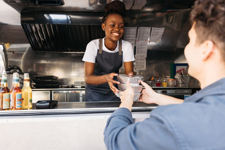 Young woman in apron working at food truck  Small business owner giving takeaway packaged food to customer