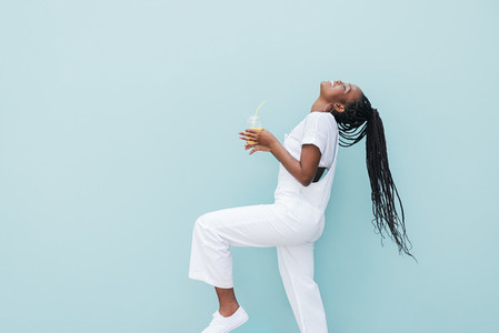 Side view of woman in white clothes having fun against blue wall  Young female holding a juice enjoying good mood