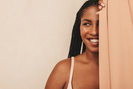 Carefree young woman smiling behind a studio curtain