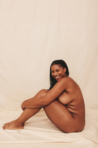 Young woman smiling while sitting nude in a studio