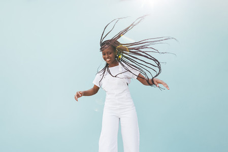 Happy woman in casuals making her long braided hair fly in air at wall