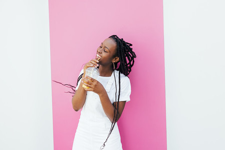 Happy woman drinking juice while dancing at white wall with pink stripe