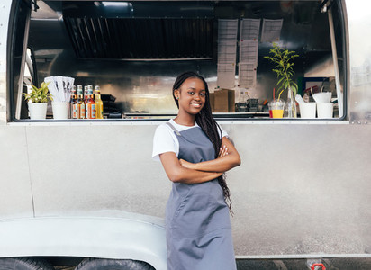 Confident woman in apron standing at her food truck with crossed arms