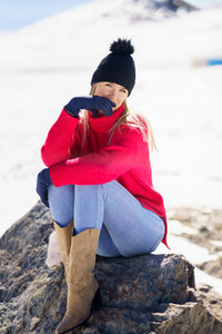Young woman sitting on a rock in the snowy mountains in winter in Sierra Nevada Granada Spain