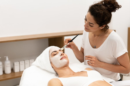 Aesthetics applying a mask to the face of a Middle aged woman in modern wellness center