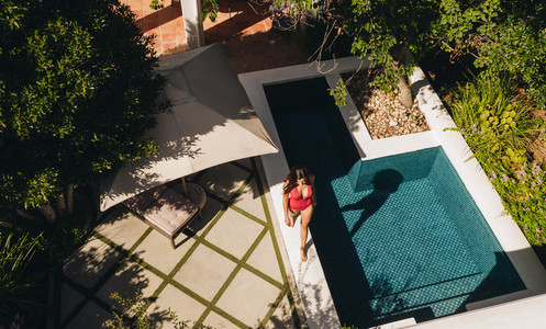 Aerial view of a young woman walking next to a pool in a swimsui