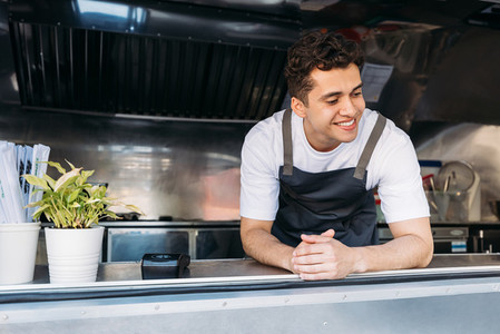 Handsome food truck owner in apron leaning on the counter looking down
