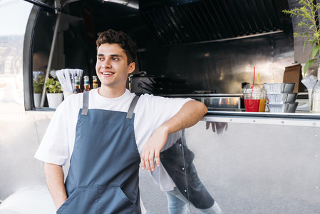 Portrait of young waiter leaning on food truck counter and smiling