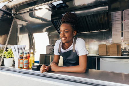 Smiling saleswoman in apron leaning counter standing in a food truck