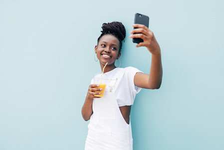 Happy woman in white casuals taking selfie holding orange juice