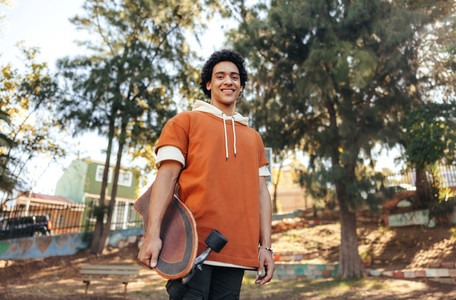Carefree skateboarder holding his skateboard in an urban park
