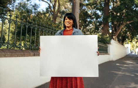 Smiling woman holding a blank placard outdoors