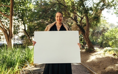 Cheerful posh woman holding up a white placard outdoors