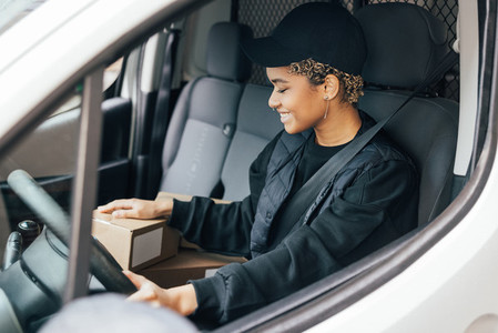 Smiling woman courier sitting on a driver seat checking boxes for delivery