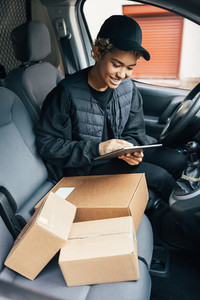 Female courier preparing packages for transportation while sitting on drivers seat