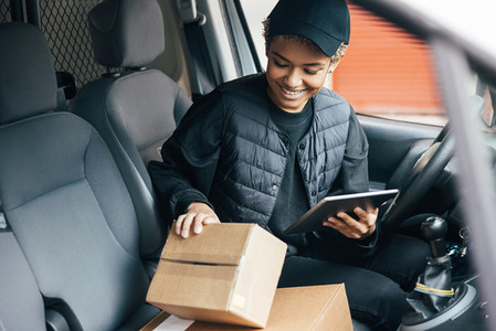 Young smiling woman in uniform checking the package for delivering in car