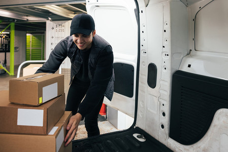 Smiling male courier working in warehouse upload boxes into a van for delivery