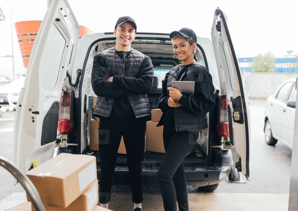 Portrait of confident delivery man and woman in uniform standing against a van