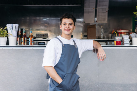 Portrait of a confident waiter leaning on a food truck looking at camera